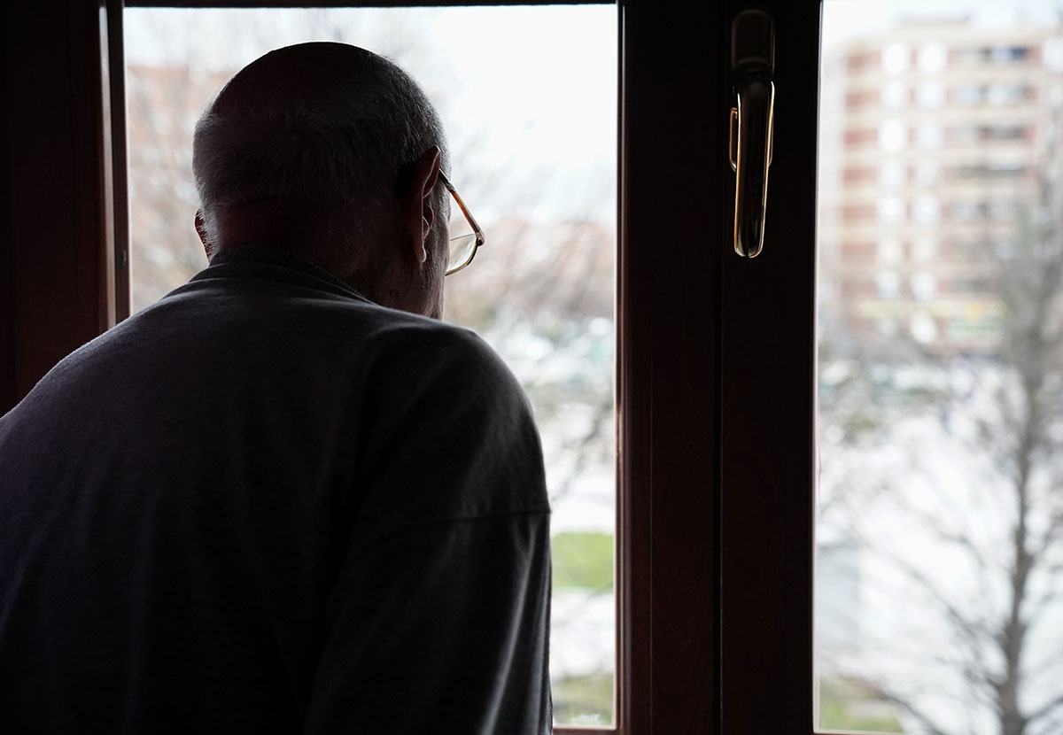 Ensam äldre man tittar ut genom ett fönster