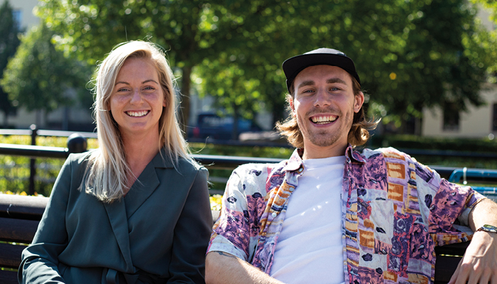 Två studentguider sittandes på en bänk utomhus vid Högskolan i Gävle. Sommar.